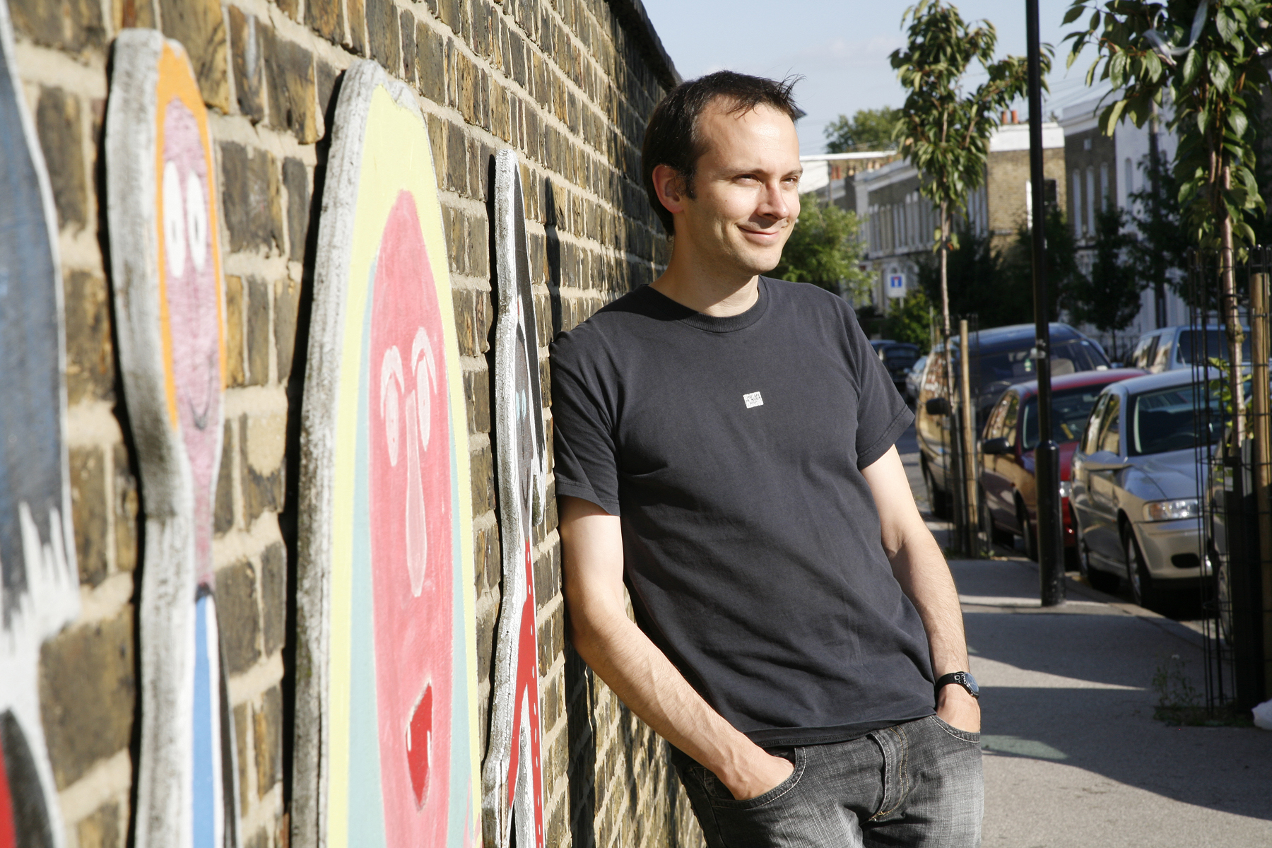 Tim Harford in black t-shirt and jeans, leaning against a wall with murals