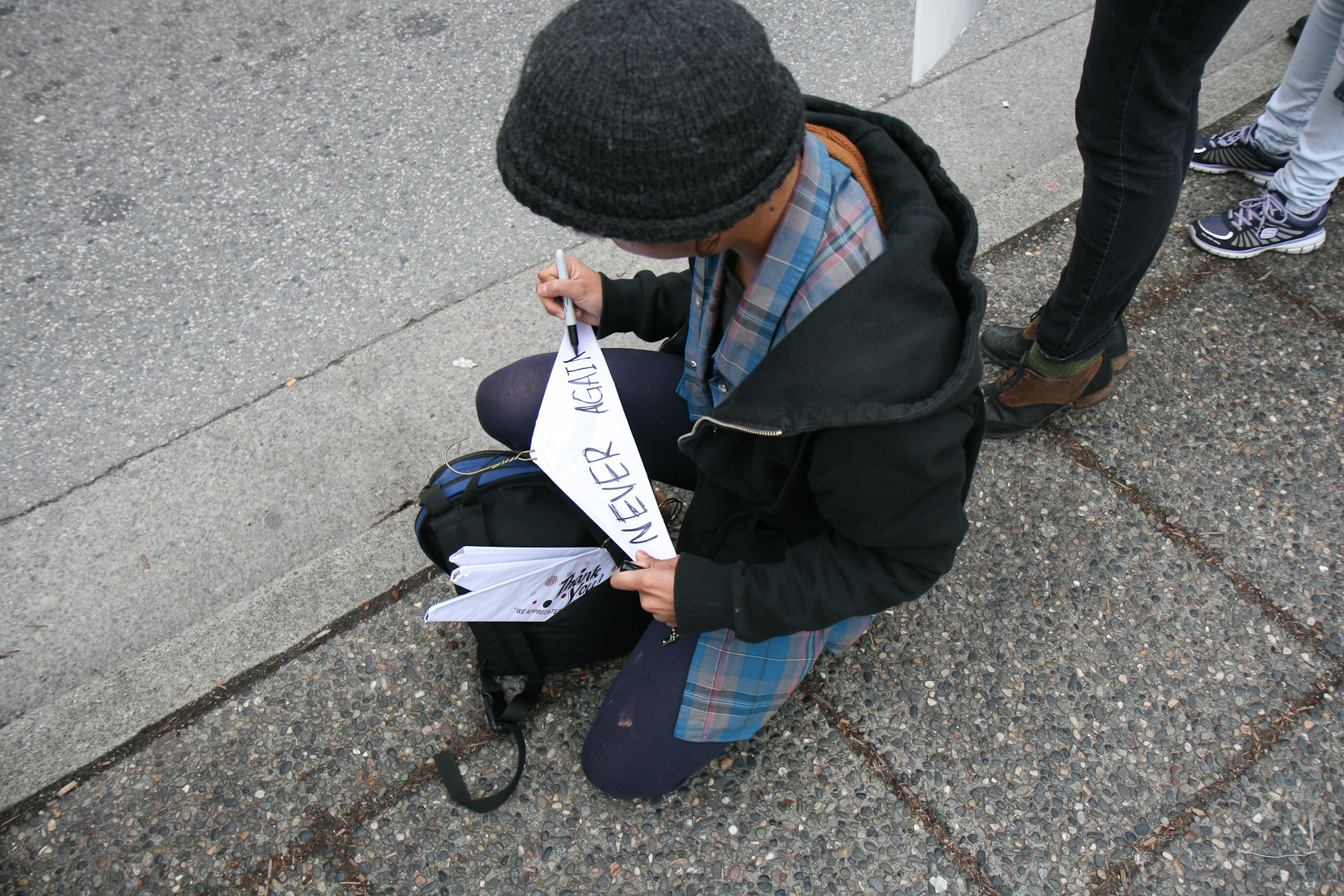 A person in a beanie writes "never again" on a coat hanger