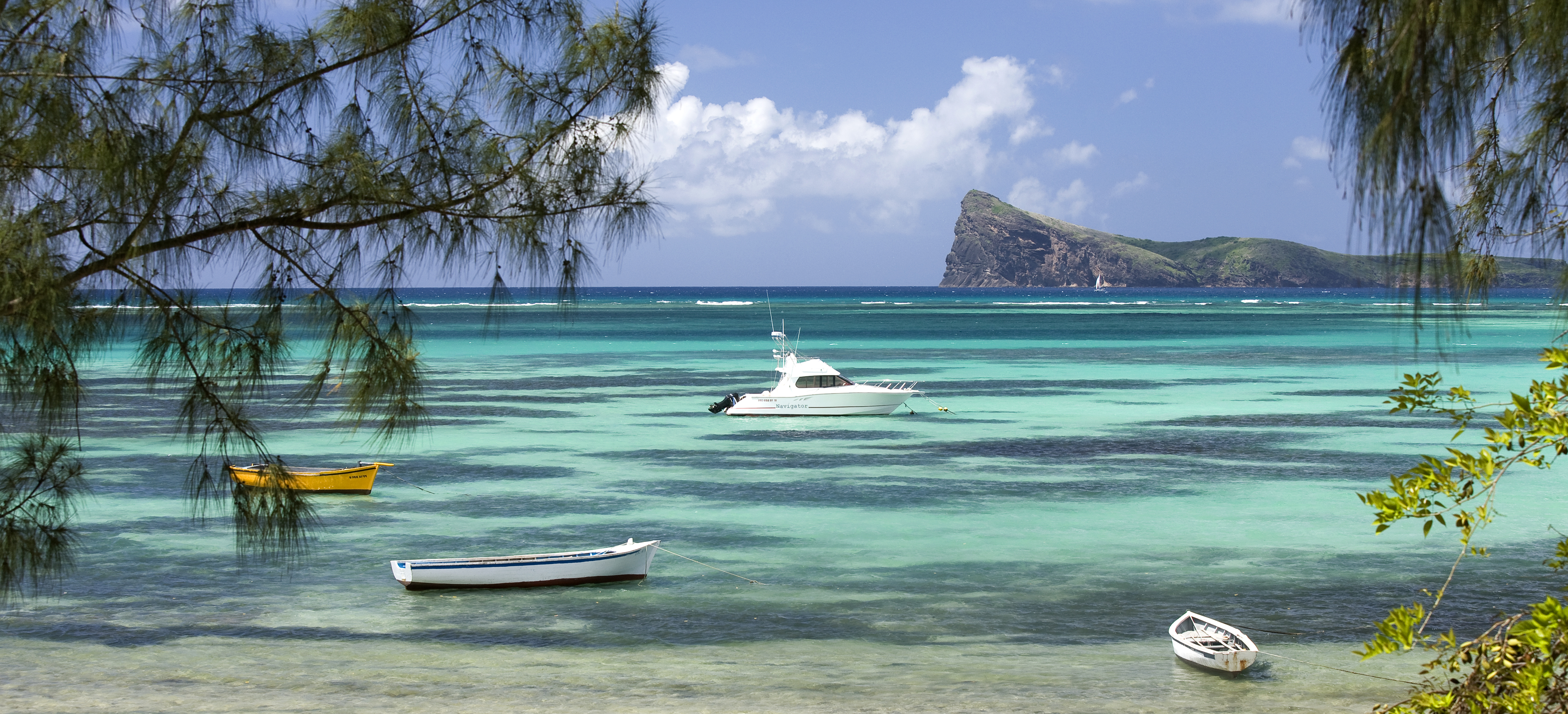 A beach, with aquamarine water and blue skies; four boats