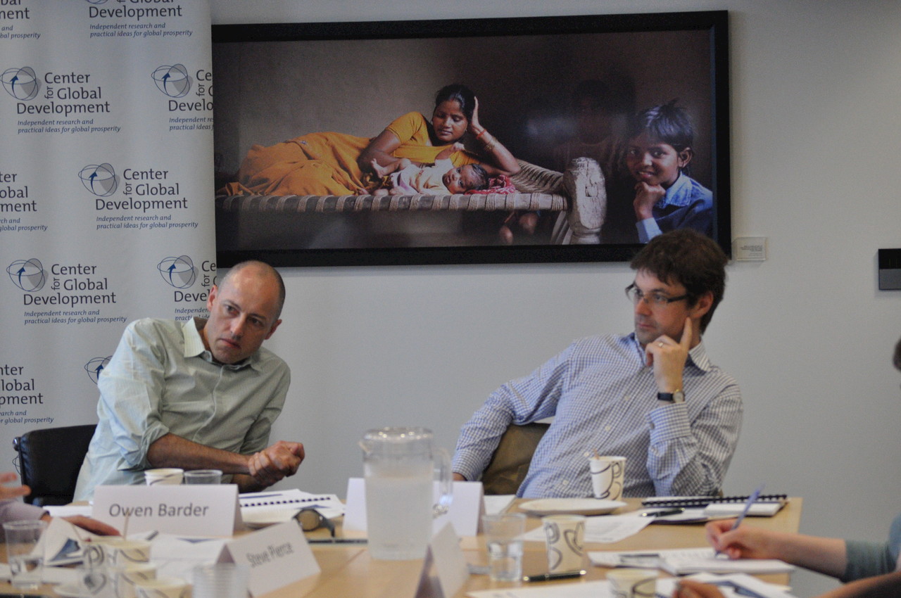 Owen Barder and Toby Eccles at the end of a conference table, with a picture of children behind them