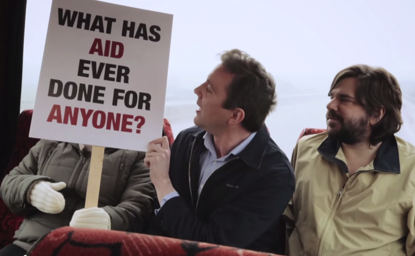 A man holding a sign saying "what has aid ever done for anyone?"