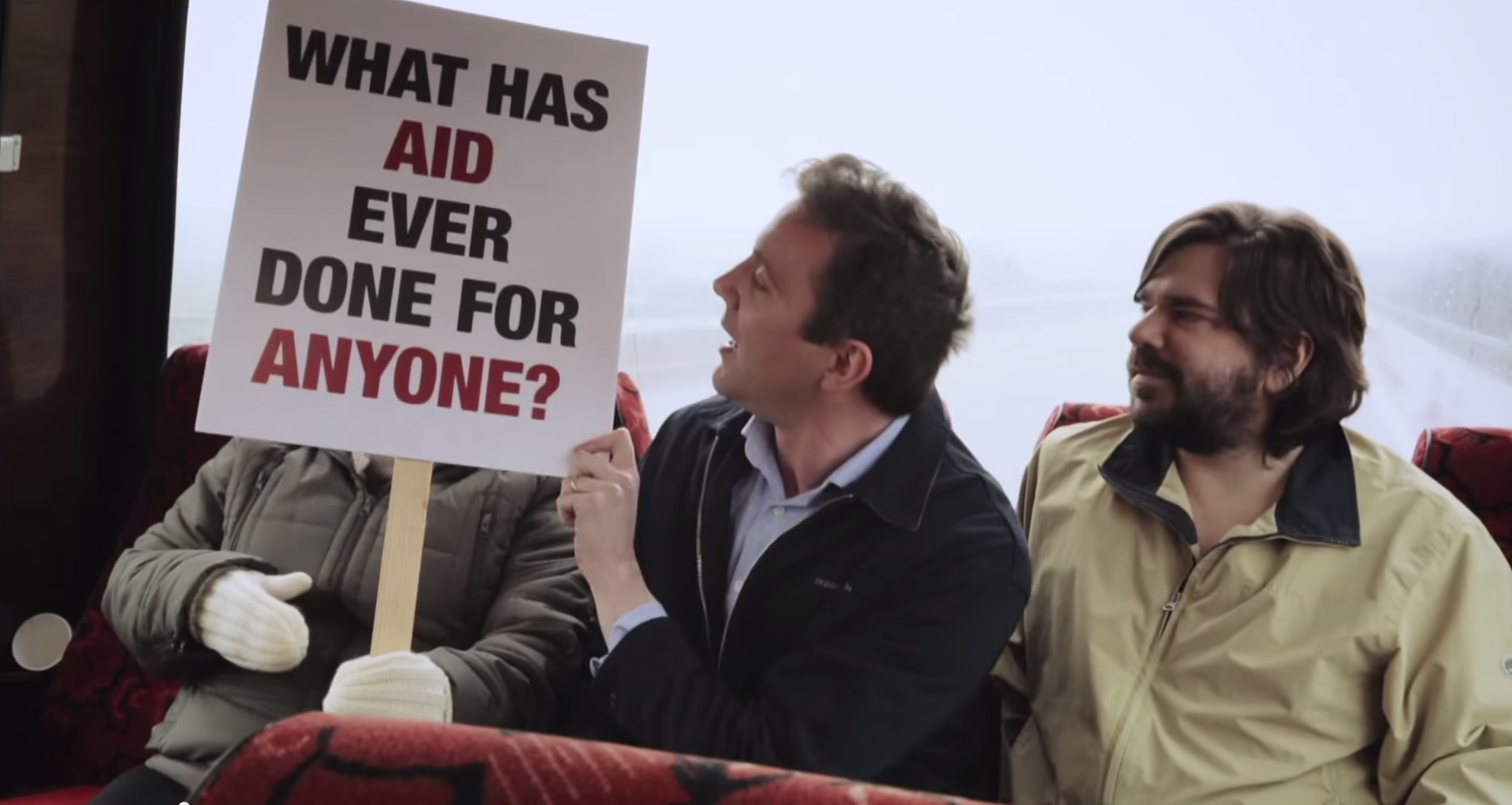 A man holding a sign saying "what has aid ever done for anyone?"